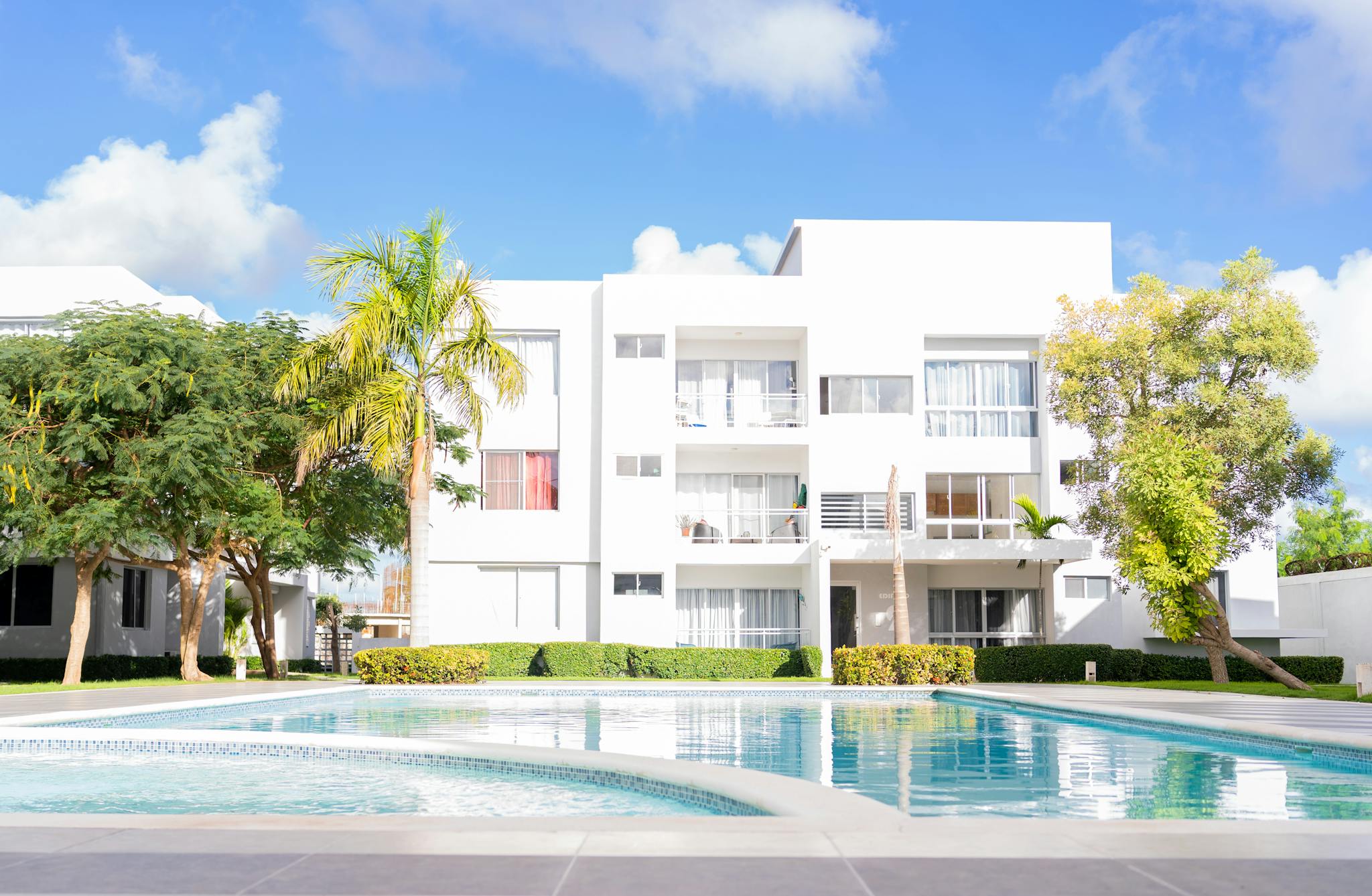 Beautiful view of a modern white apartment building with a surrounding outdoor pool under a clear blue sky.